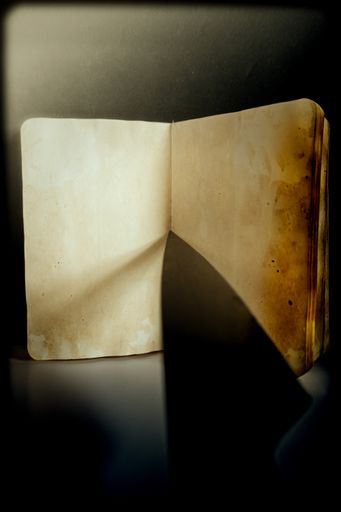A vertical shot of an old wethered blank dairy notebook with a sharp knife tip pointing on it