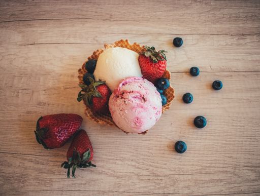 A top view of two scoops of strawberry and vanilla ice cream in a waffle cone on a wooden surface