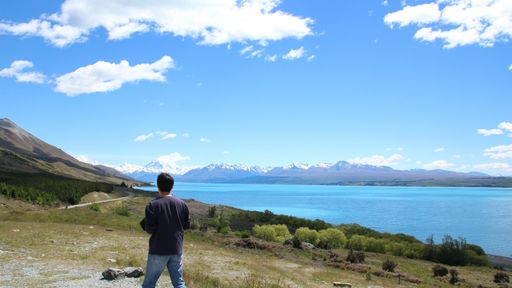 A horizontal shot of a man standing on the valley looking at the beautiful blue ocean with mountains
