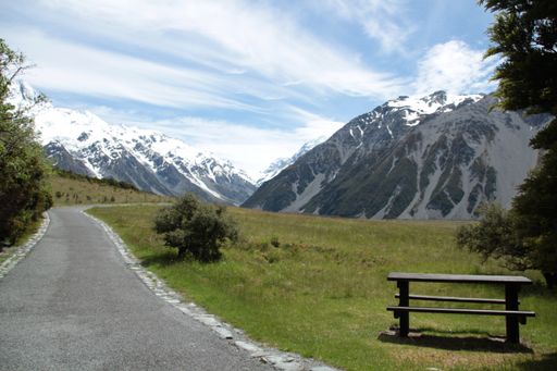 A beautiful view of the road with the bench and the trees on the mountain chain background