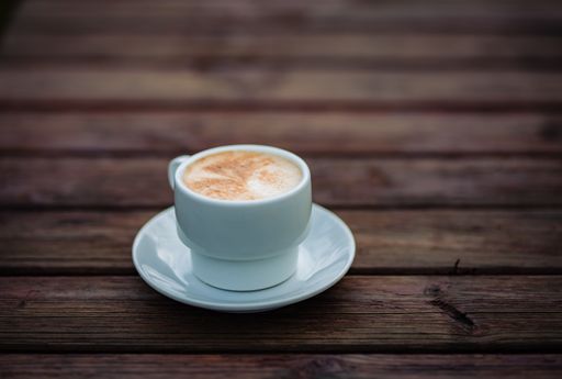 A selective focus shot of a cappuccino in a white cup on a wooden table