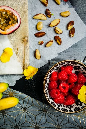 A vertical shot o berries, passion fruit, bananas, other tropical fruits, nuts on a chopping board