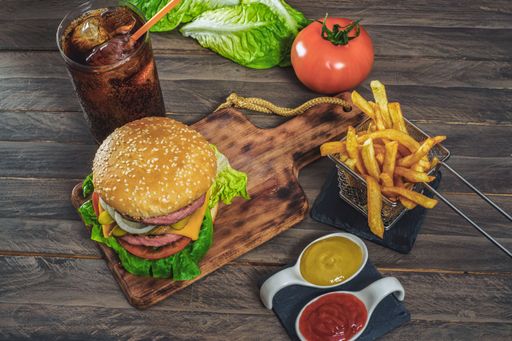 hamburger complete with two meats, sauces, french fries and cola on an antique wooden board.