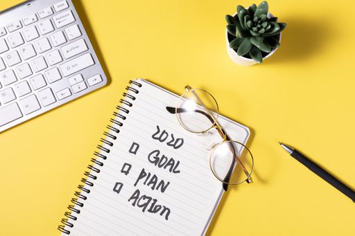 A flat lay of a notepad with a motivational schedule written on it on yellow background