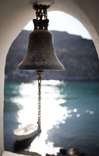 A vertical shallow focus of a hanging vintage bell with a sparkling sea on the background
