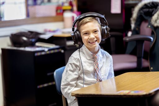 A selective focus shot of a cheerful boy wearing headphones sitting in the classroom