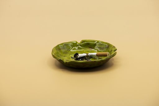 A shot of a cigarette in green ceramic ashtray on beige background - the concept of quitting smoking