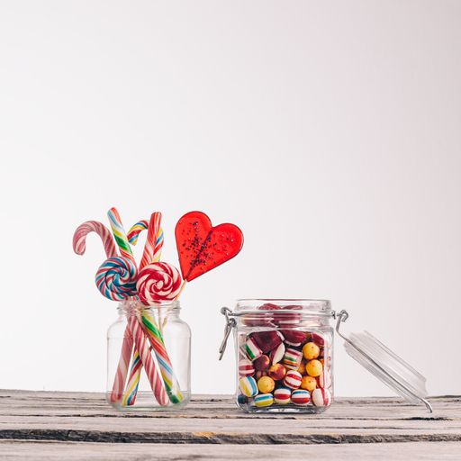 A closeup shot of candy canes and other candies in glass jars on a wooden surface - perfect for a cool wallpaper