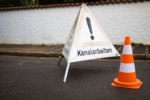 The warning sign and a traffic cone on the street
translation: Sewer works