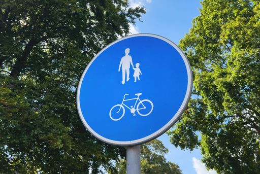 A blue road sign featuring a bicycle and people walking with green trees on the background