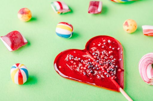 A closuep shot of a heart-shaped lollipop and other candies on a green surface