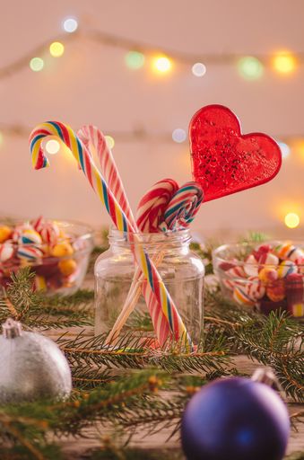 A vertical closeup shot of candy canes and spruce tree branches on a wooden surface with Christmas lights in the background
