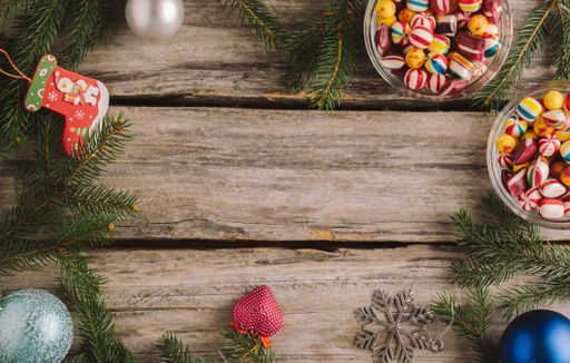 A high angle shot of candies, Christmas baubles and spruce tree branches on a wooden surface