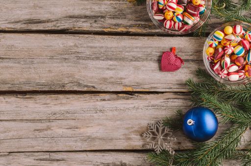A high angle shot of candies, Christmas baubles and spruce tree branches on a wooden surface