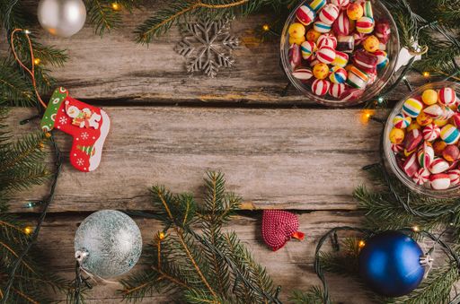 A high angle shot of candies, Christmas baubles and spruce tree branches on a wooden surface