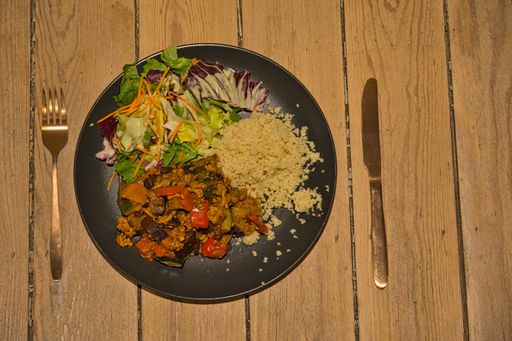 A top shot of vegan goulash with couscous and salad on a wooden table with fork and knife
