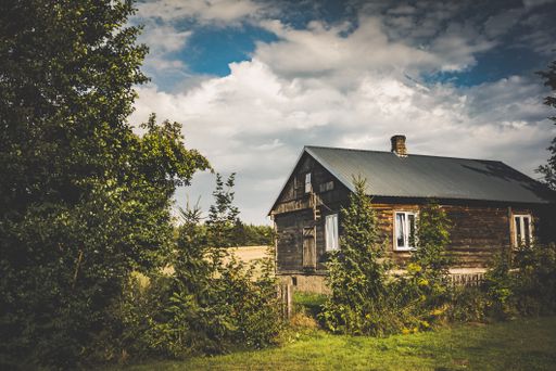 A wooden house surrounded by greenery under the sunlight and a cloudy sky in the countryside