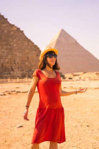 A pregnant Caucasian tourist in red dress posing in front of the great pyramids of Giza in Egypt