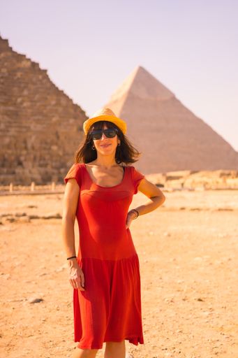 A pregnant Caucasian tourist in red dress posing in front of the great pyramids of Giza in Egypt