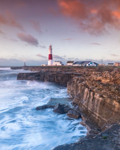 The Portland Bill lighthouse in Portland, Dorset, UK with the colors of sunrise and the waves made for a lovely swell