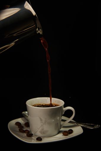 A vertical shot of hot fresh coffee pouring from a pot into a cup isolated on a black background