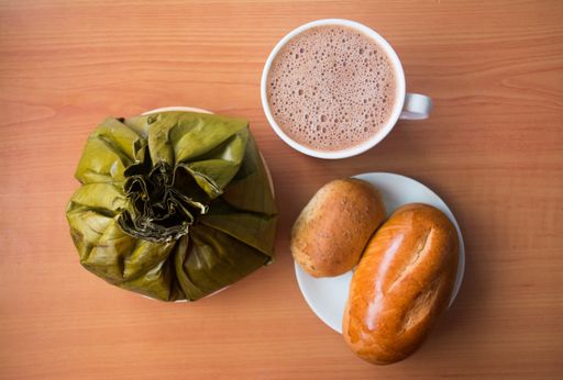 A top view of delicious colombian tamales, with fresh bread and coffee on a wooden surface
