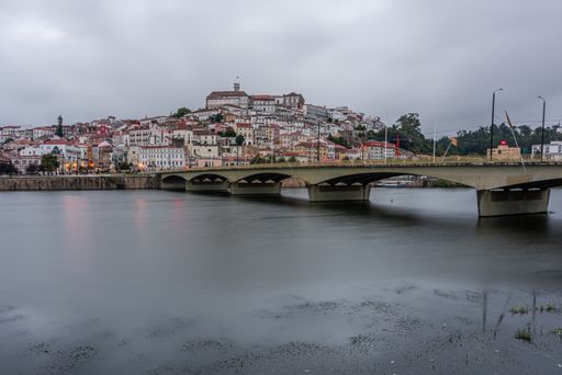 A bridge in the sea surrounded by the Coimbra city under a cloudy sky in Portugal