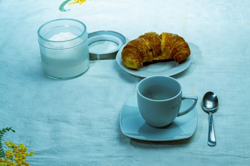 A top view closeup of a croissant on a white plate next to a container with powdered sugar and coffee