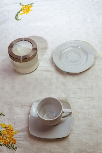A top view closeup of an empty white plate, a container with sugar and an empty coffee cup on a table