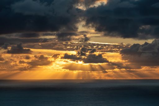 View of dark clouds lit by bright sunset light with fading blue sky above