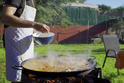 A Caucasian male preparing Valencian paella in the garden