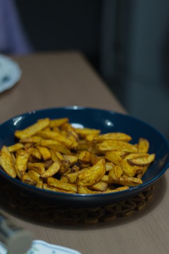 A vertical shot of french fries in a bowl on the table in the kitchen. Potatoes cut in a fry shape