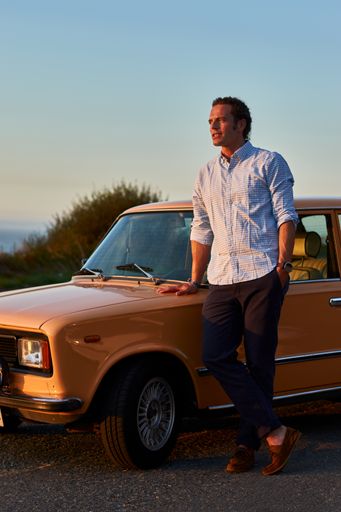 A vertical shot of nicely dressed man standing by his old vintage car looking at the lake