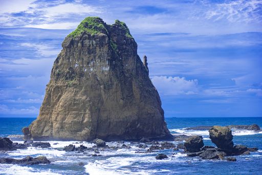 An immense rock formation in wavy seawater under a majestic cloudscape