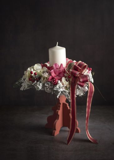 A beautiful closeup of a Christmas white candle with ribbons and branches on a grey background