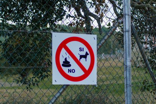 A white banner on the netted fence with a red sign - dogs are allowed, pooping is banned