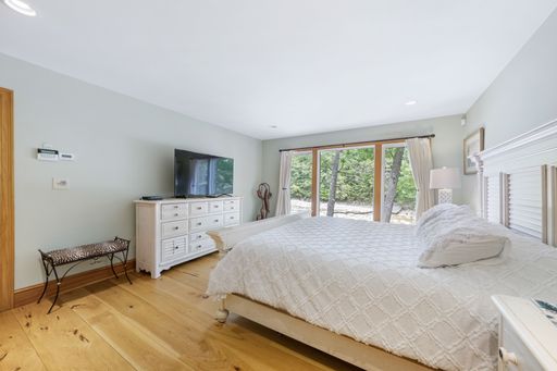 An interior shot of a bedroom with a bed with white sheets, light green walls and a TV.