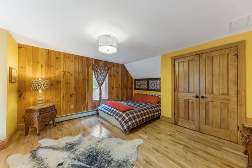 An interior shot of a wooden bedroom with a white ceiling and a decorative carpet.