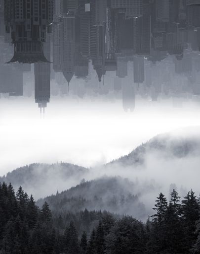 A grayscale of an urban skyline with smog clouds displayed over misty mountain scenery