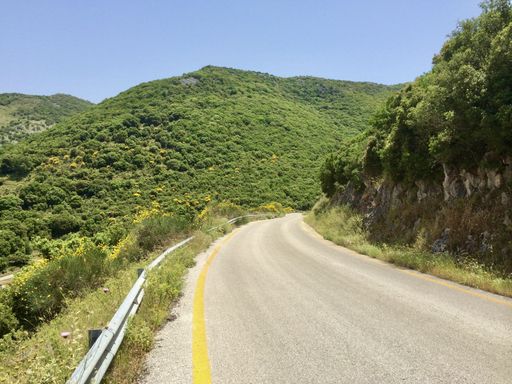 A beautiful shot of a rural car road going down with mountains, trees, and cliffs on the side