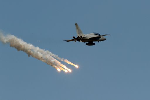 A jet aircraft flying in the sky and fireworks smoking below