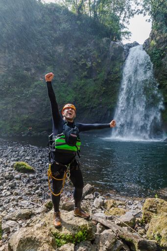 A vertical shot of a Hispanic cheerful rock climber in a helmet hat and safety harness celebrating an achievement