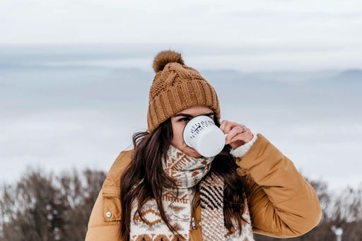 A young Caucasian woman wearing warm clothes and drinking tea outside