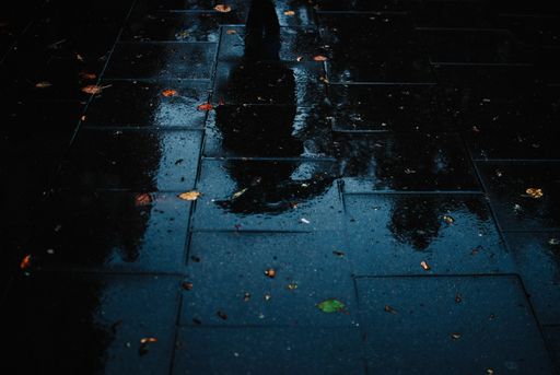 The blurry reflection of a person on the wet sidewalk