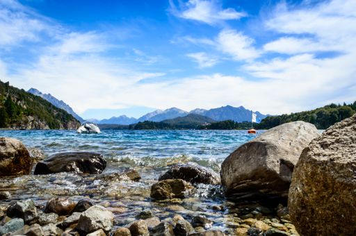 The rocks from the shore of a lake in summer. Pines, mountains, crystal clear water.