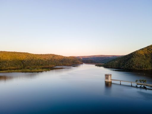 A mesmerizing view of calm lake water surrounded by green mountains and trees against a clear sky