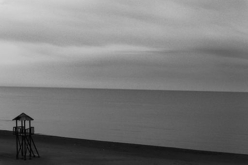 A grayscale shot of the tranquil sea under a cloudy sky on a gloomy day