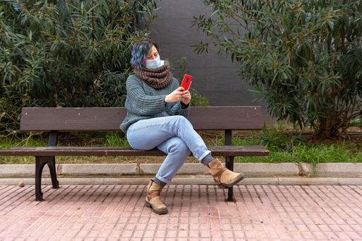 A stylish lady with colorful hair using her phone in a park wearing a sanitary mask