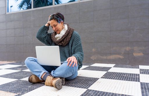 A stylish young lady with colorful hair sitting on a checkered floor in a park using her laptop