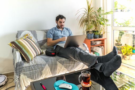 A Caucasian man with a cup of tea working with his laptop in the living room - the concept of online working